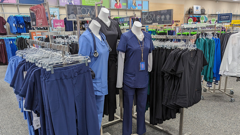 Mannequins wearing Cherokee uniforms and scrubs in navy blue, ceil blue and black. A wide selection of Healing Hands and Med Couture is visible in the background. 